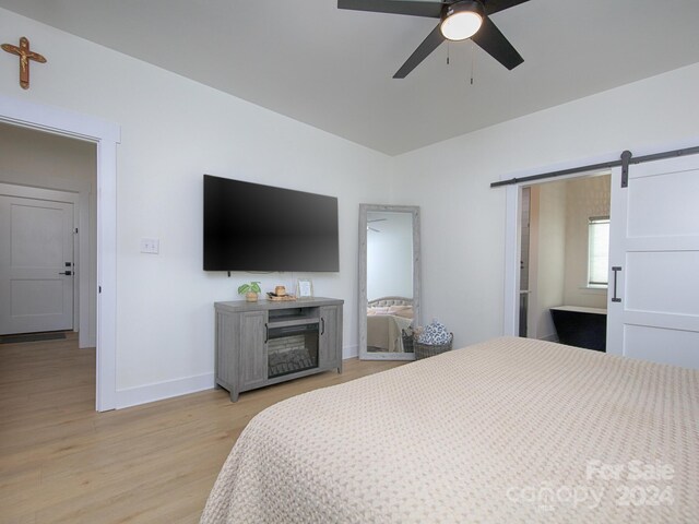 bedroom with a barn door, light hardwood / wood-style floors, and ceiling fan