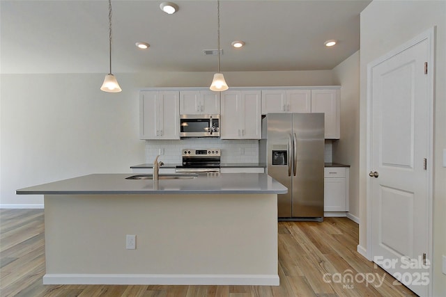 kitchen featuring appliances with stainless steel finishes, sink, decorative light fixtures, a center island with sink, and white cabinetry