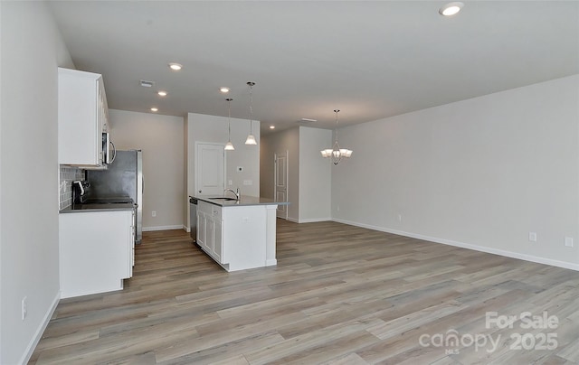 kitchen with white cabinets, an island with sink, hanging light fixtures, and an inviting chandelier