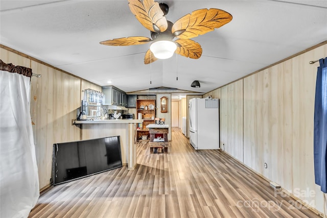 living room featuring ceiling fan, wood walls, vaulted ceiling, and light hardwood / wood-style flooring