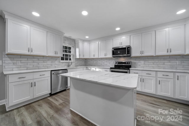 kitchen featuring appliances with stainless steel finishes, light stone counters, light hardwood / wood-style flooring, a center island, and white cabinetry