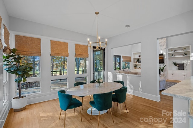 dining area featuring light hardwood / wood-style flooring, built in features, and a notable chandelier