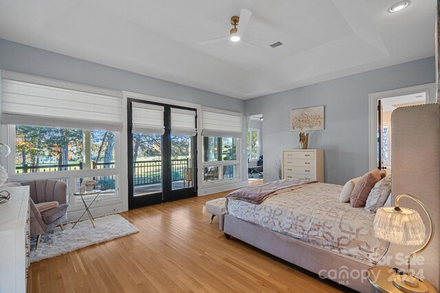 bedroom featuring access to outside, ceiling fan, hardwood / wood-style floors, and a tray ceiling