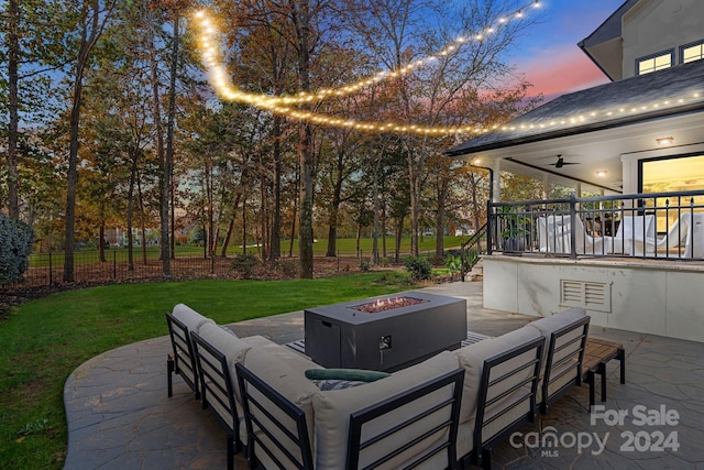 patio terrace at dusk with a lawn, ceiling fan, and an outdoor living space with a fire pit