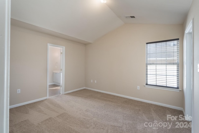 unfurnished bedroom with light carpet, vaulted ceiling, and ensuite bath