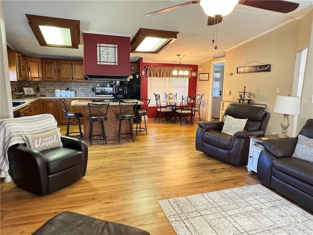 living room featuring ceiling fan with notable chandelier, vaulted ceiling, ornamental molding, and light hardwood / wood-style flooring