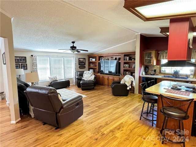 living room with ceiling fan, light wood-type flooring, a textured ceiling, and vaulted ceiling