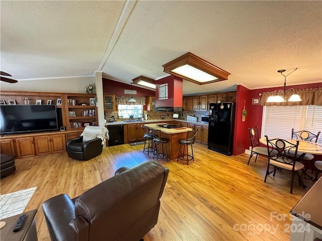 living room with ornamental molding, light wood-type flooring, vaulted ceiling, and a healthy amount of sunlight