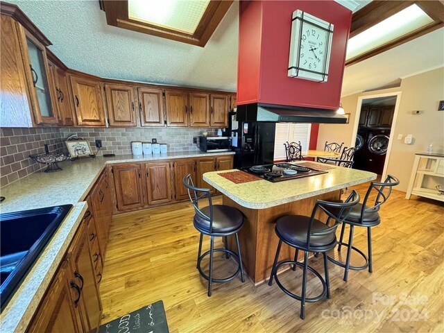 kitchen featuring black appliances, a breakfast bar, exhaust hood, and light hardwood / wood-style flooring