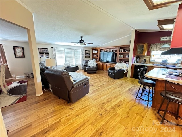 living room featuring light wood-type flooring, ornamental molding, a textured ceiling, ceiling fan, and lofted ceiling