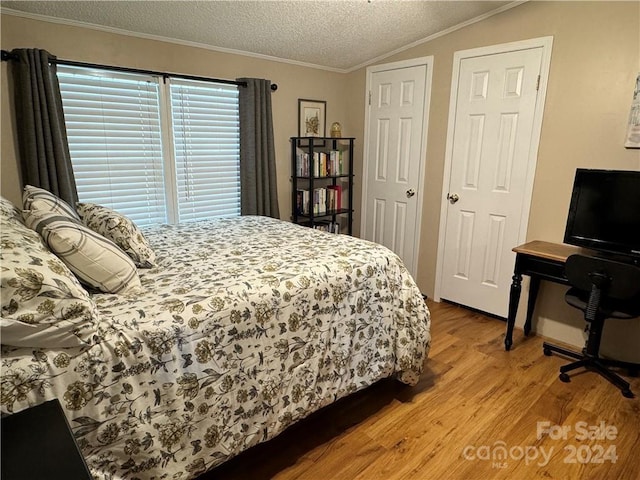 bedroom featuring lofted ceiling, crown molding, light hardwood / wood-style flooring, and a textured ceiling