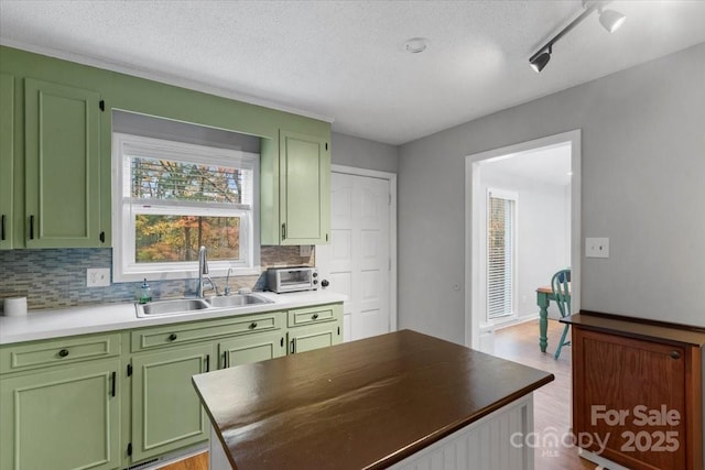 kitchen with sink, a textured ceiling, green cabinetry, decorative backsplash, and light wood-type flooring