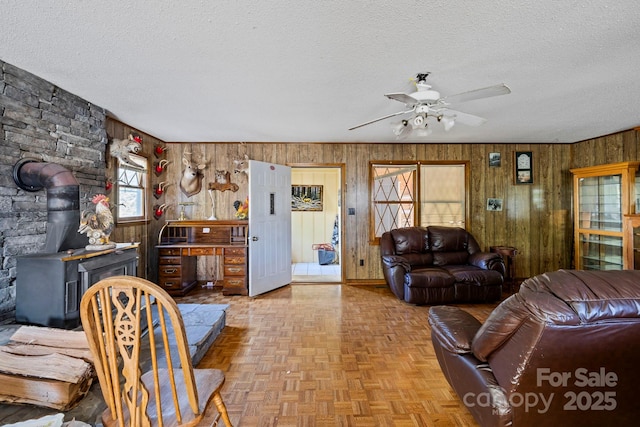 living room with light parquet floors, a textured ceiling, a wood stove, and ceiling fan