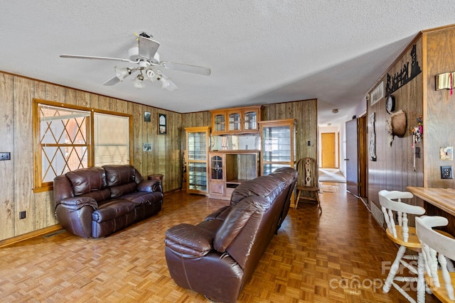 living room with parquet flooring, a textured ceiling, ceiling fan, and wooden walls