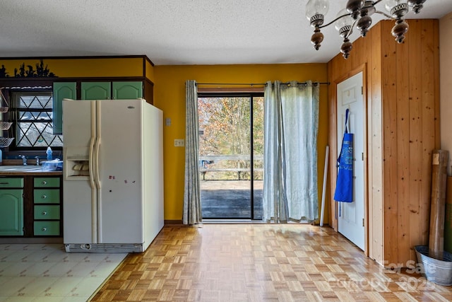 kitchen featuring sink, green cabinets, white refrigerator with ice dispenser, a textured ceiling, and wooden walls