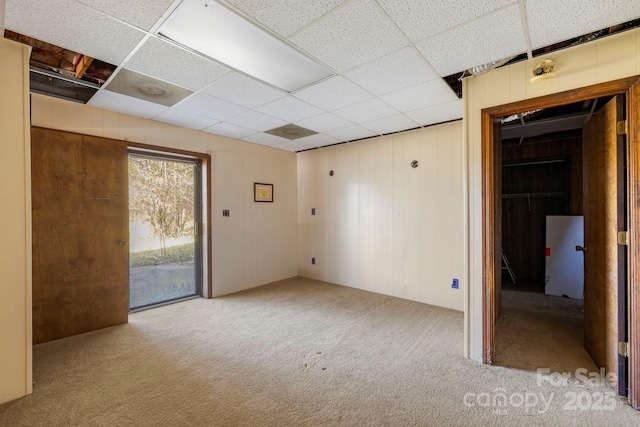 carpeted spare room featuring a drop ceiling and wood walls