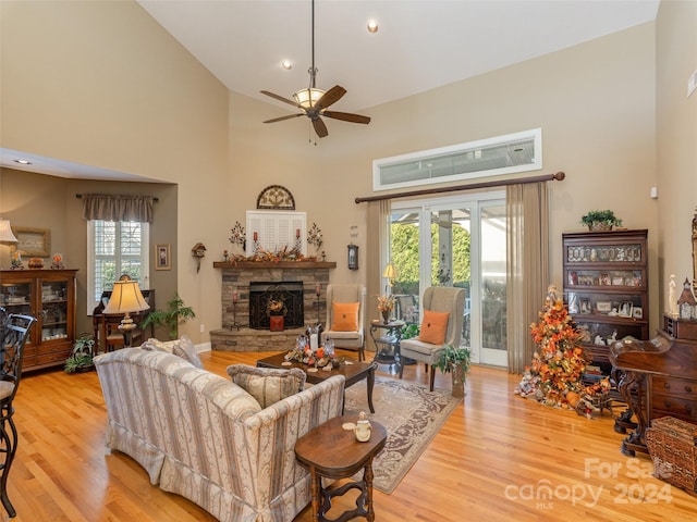 living room with light hardwood / wood-style floors, high vaulted ceiling, ceiling fan, and a stone fireplace