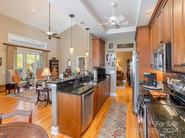 kitchen featuring sink, stainless steel appliances, dark stone counters, decorative light fixtures, and light hardwood / wood-style floors