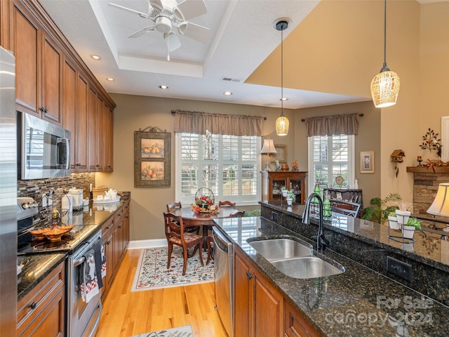 kitchen featuring light wood-type flooring, dark stone counters, stainless steel appliances, sink, and pendant lighting