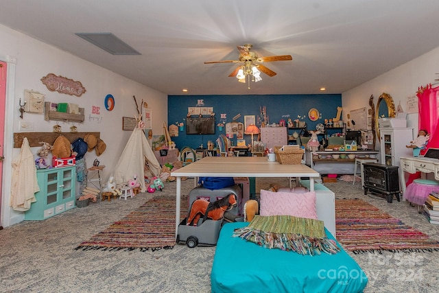 game room with ceiling fan, carpet floors, and a wood stove