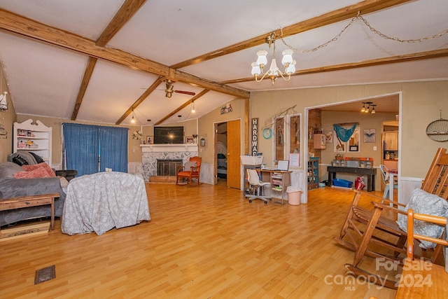 living room with hardwood / wood-style flooring, vaulted ceiling with beams, a stone fireplace, and an inviting chandelier