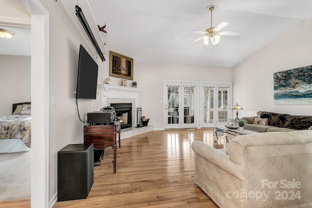 living room featuring ceiling fan, light hardwood / wood-style floors, a tile fireplace, and vaulted ceiling