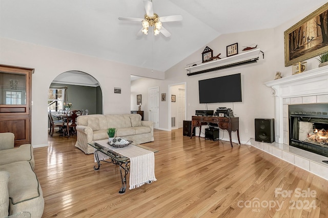 living room with ceiling fan, a tiled fireplace, light hardwood / wood-style flooring, and vaulted ceiling