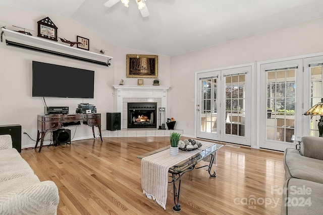 living room with ceiling fan, a tiled fireplace, light hardwood / wood-style flooring, and vaulted ceiling