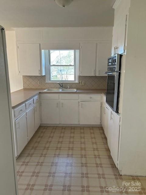 kitchen with sink, white cabinets, tasteful backsplash, wall oven, and stainless steel fridge