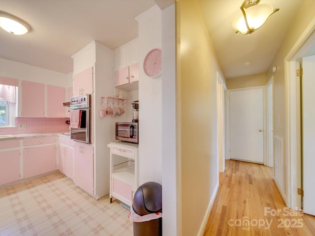 kitchen featuring appliances with stainless steel finishes, white cabinetry, backsplash, and light hardwood / wood-style flooring