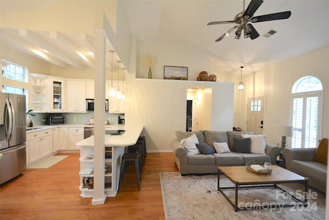 living room with light wood-type flooring, high vaulted ceiling, ceiling fan, and a healthy amount of sunlight