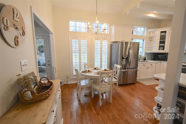 dining space with beam ceiling, light hardwood / wood-style flooring, a chandelier, and sink