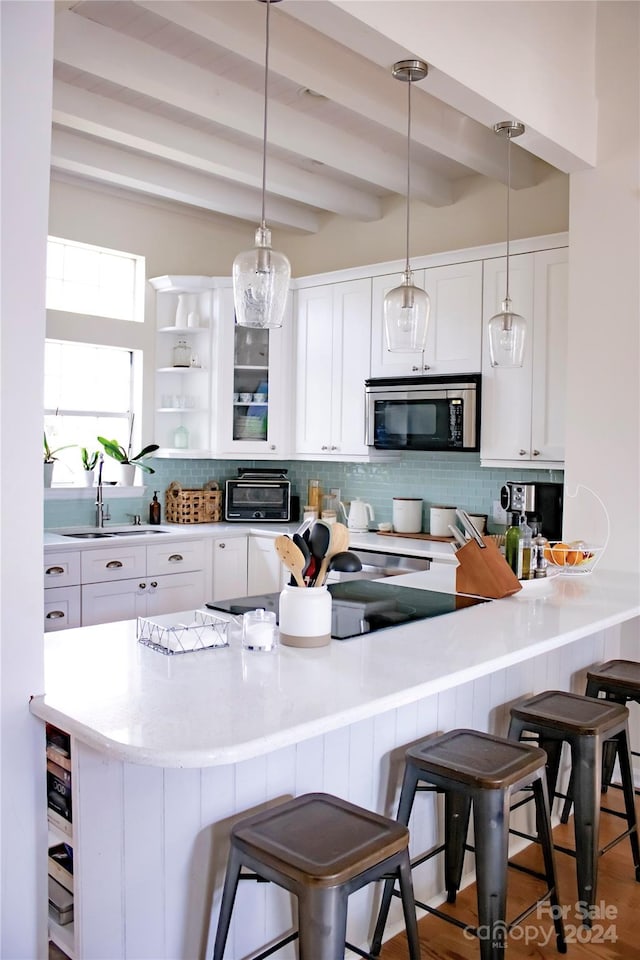 kitchen with a kitchen bar, sink, decorative light fixtures, beamed ceiling, and white cabinets