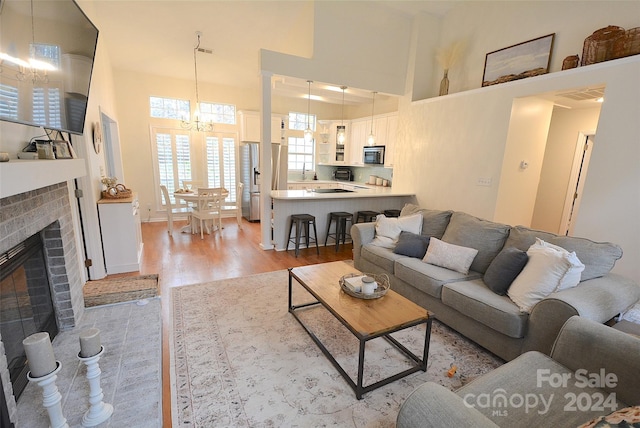 living room with a chandelier, light wood-type flooring, a high ceiling, and a brick fireplace