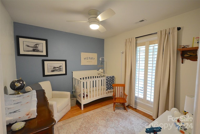 bedroom featuring ceiling fan, light hardwood / wood-style floors, and a crib