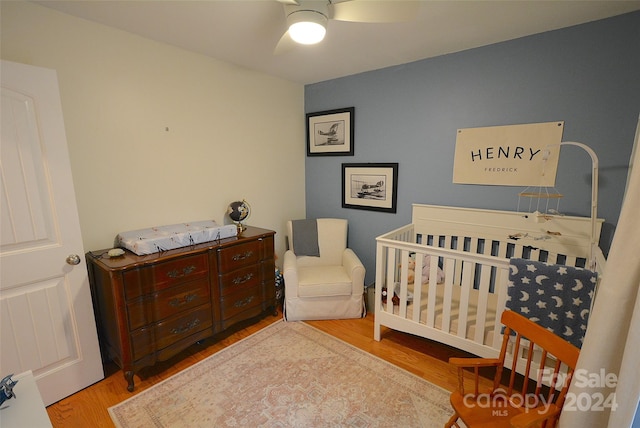 bedroom featuring ceiling fan, a crib, and light wood-type flooring