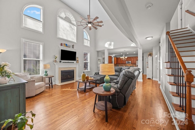 living room featuring ceiling fan with notable chandelier, a towering ceiling, and light hardwood / wood-style flooring