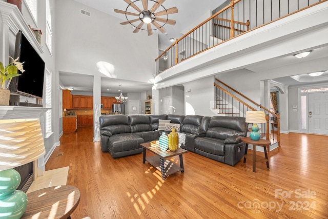 living room with light hardwood / wood-style flooring, a towering ceiling, and ceiling fan with notable chandelier