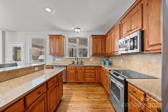 kitchen with light stone countertops, appliances with stainless steel finishes, decorative backsplash, sink, and light hardwood / wood-style flooring