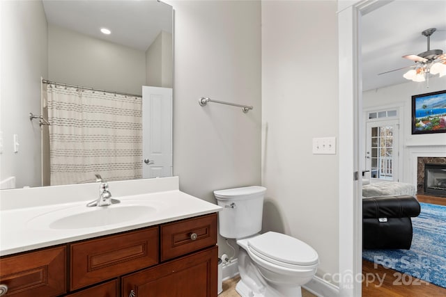 bathroom featuring vanity, ceiling fan, wood-type flooring, a fireplace, and toilet