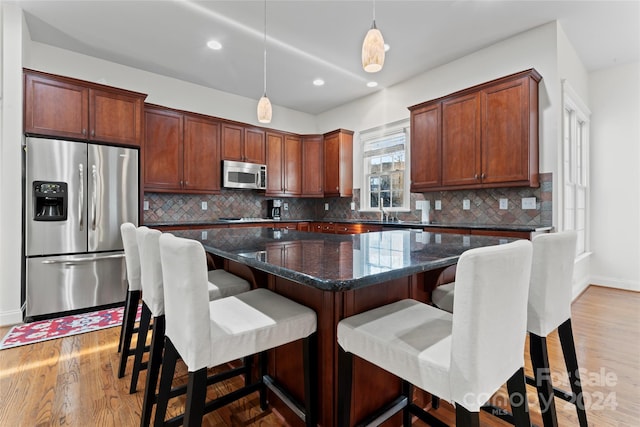 kitchen with decorative backsplash, appliances with stainless steel finishes, light wood-type flooring, pendant lighting, and a center island