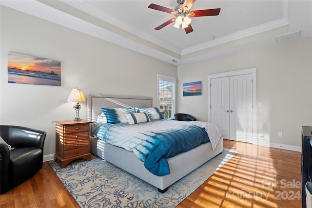 bedroom featuring hardwood / wood-style flooring, ceiling fan, ornamental molding, a tray ceiling, and a closet