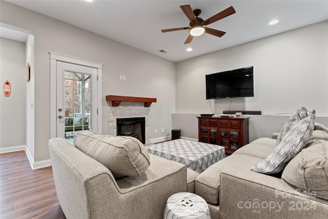 living room featuring hardwood / wood-style flooring, ceiling fan, and a stone fireplace