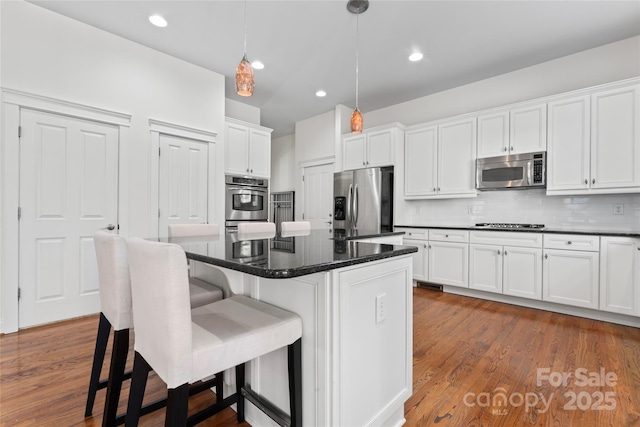 kitchen featuring white cabinets, decorative backsplash, dark wood-style floors, a breakfast bar, and stainless steel appliances