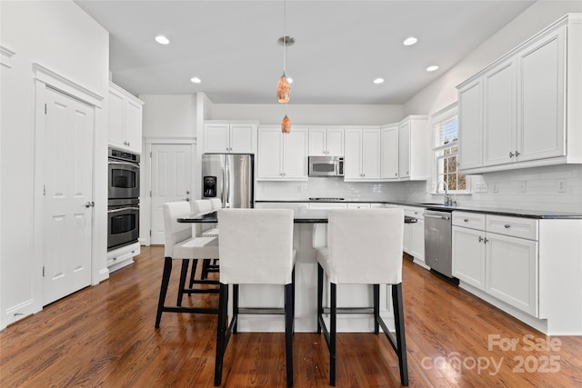 kitchen with stainless steel appliances, dark wood-type flooring, backsplash, and a kitchen bar