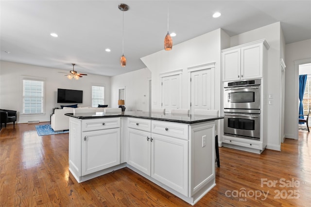 kitchen featuring white cabinets, open floor plan, dark wood-style flooring, stainless steel double oven, and recessed lighting