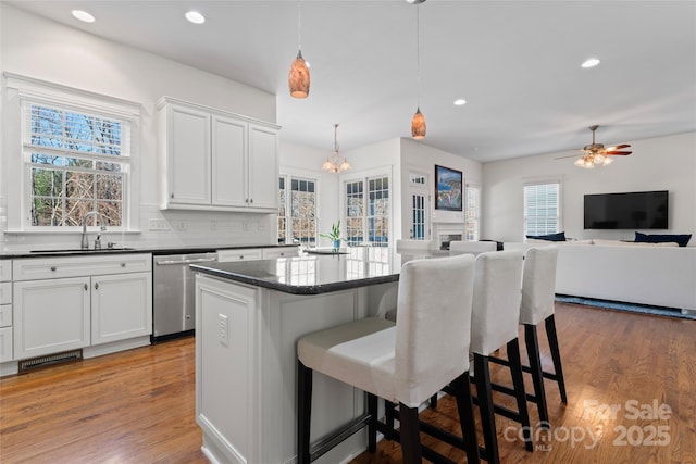 kitchen with dark countertops, wood finished floors, a center island, a sink, and stainless steel dishwasher