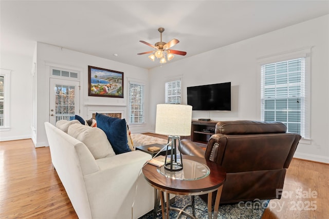 living area featuring a premium fireplace, light wood-type flooring, a wealth of natural light, and baseboards