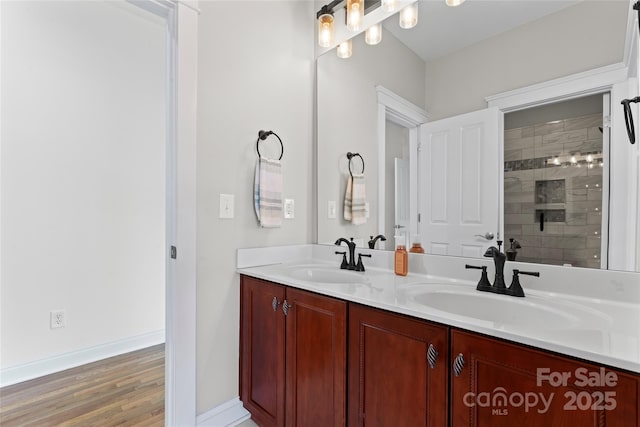 full bath featuring double vanity, tiled shower, a sink, and baseboards