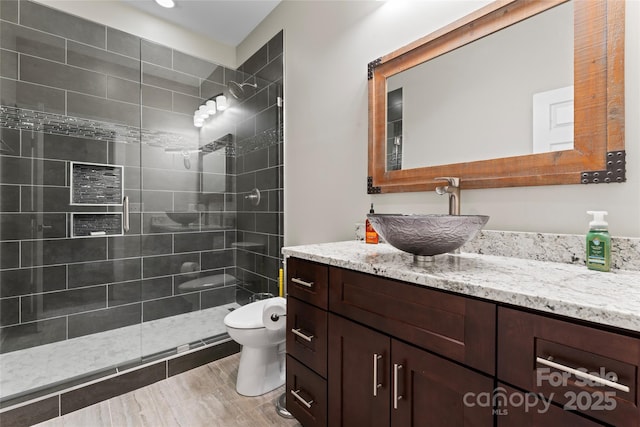 bathroom with toilet, a tile shower, and vanity